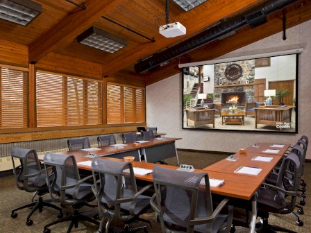 Conference room with a long table, chairs, projector, and a fireplace image on the screen.